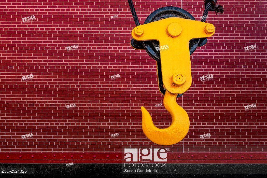 Yellow Crane Logo - Industrial Hook - Bright yellow crane hook against a red brick wall ...
