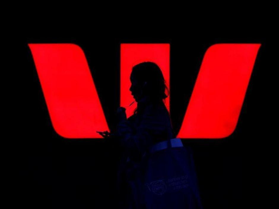 Westpac Logo - A woman walks past an illuminated logo for Australia's Westpac Bank