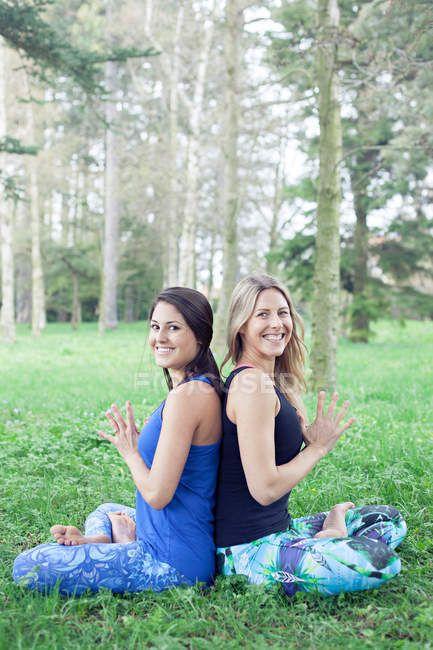 Two Women Back to Back Logo - Two women sitting in lotus pose back to back in park — sport, green ...