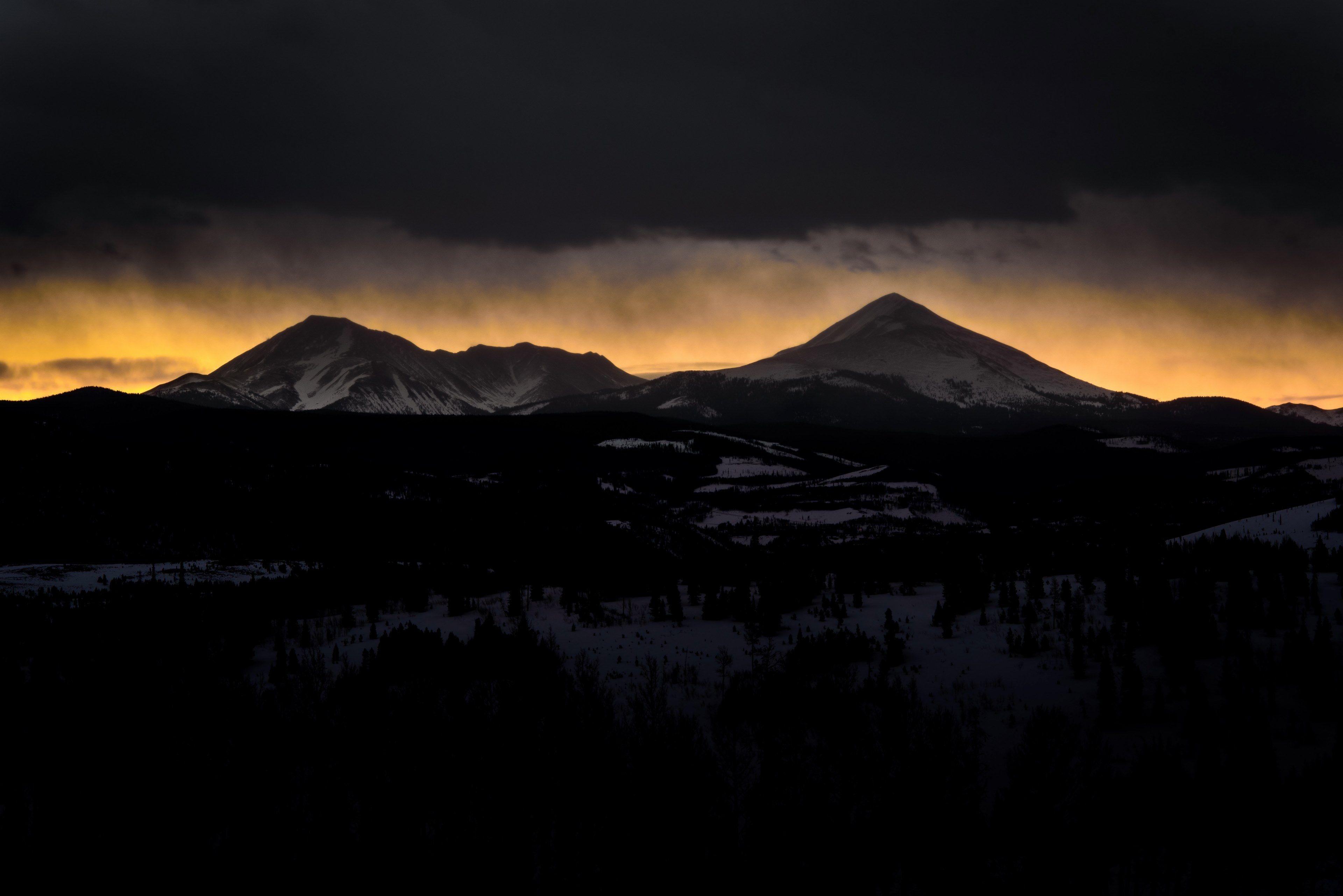 Orange Sun Behind Mountain Logo - silhouettes of snow covered mountains against the orange sunset sky